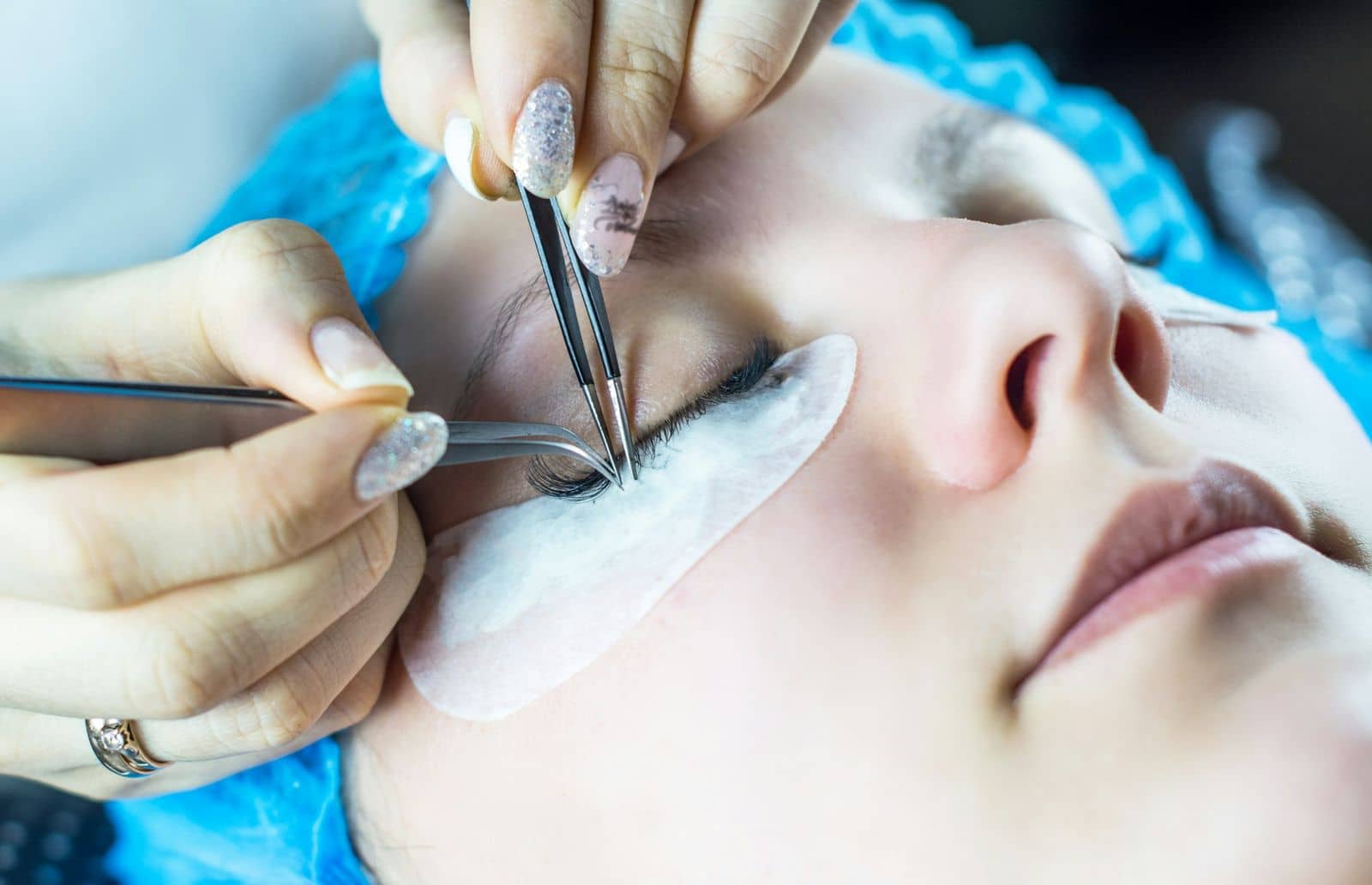 Close view of tweezers lifting a fine fan onto a client’s lashes