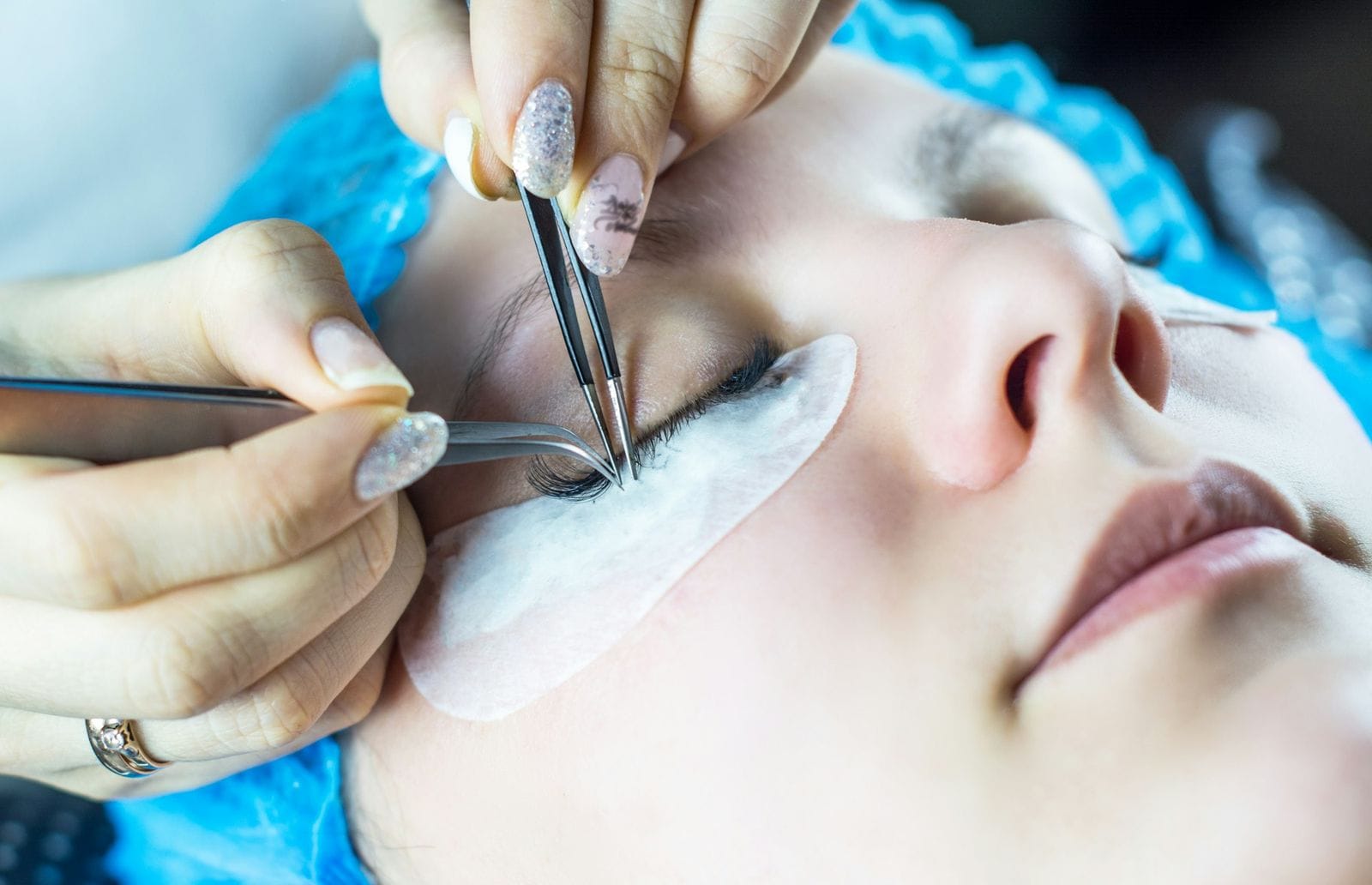 Close view of tweezers lifting a fine fan onto a client’s lashes
